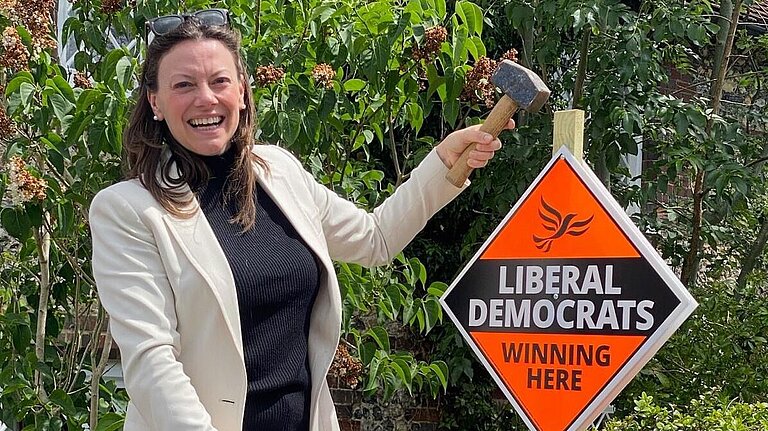 Sarah Green hammering in a Liberal Democrat Garden Poster